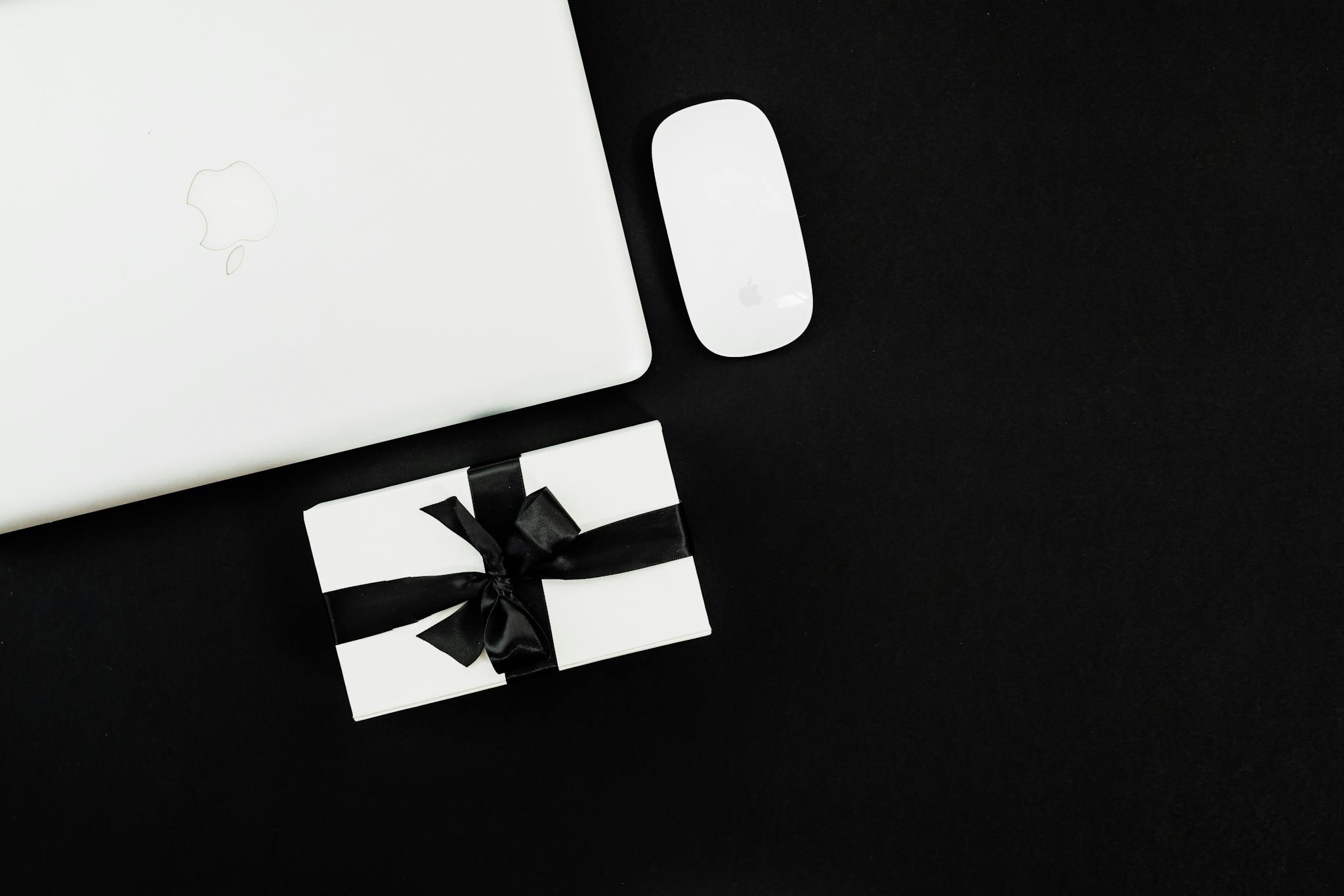 Flat lay of a laptop, mouse, and gift box, ideal for Black Friday online shopping theme.