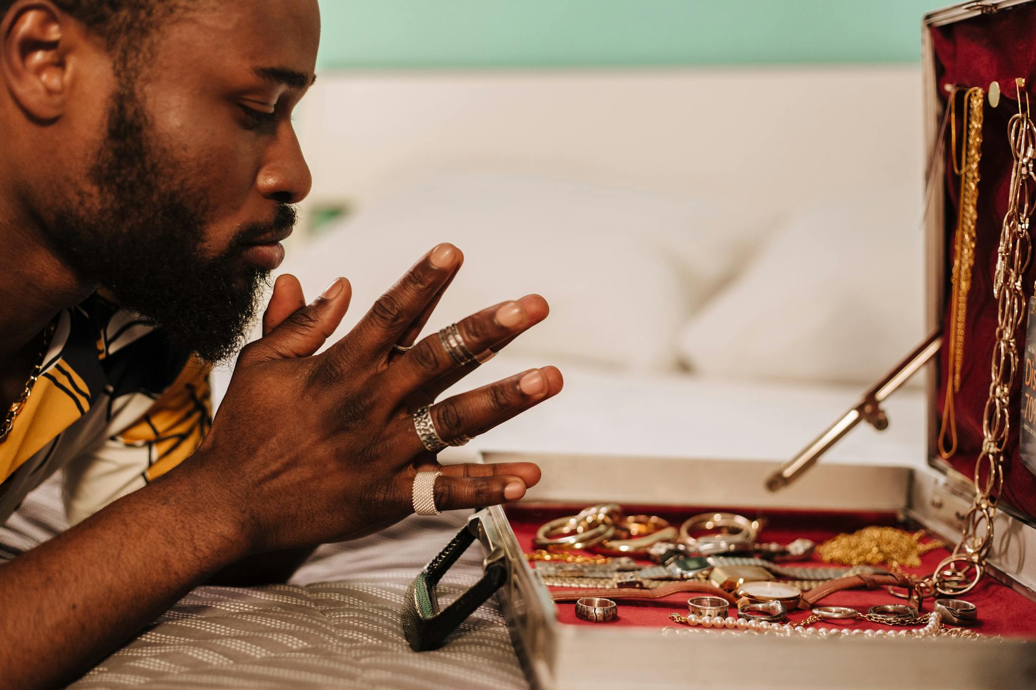 Side view of a man contemplating a collection of jewelry displayed in an open box indoors.